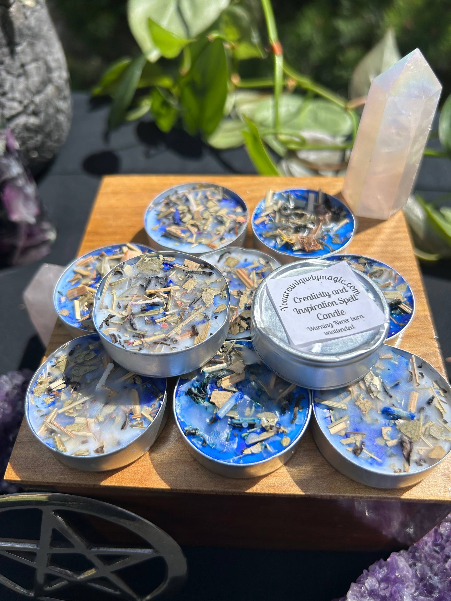 Set of small candles on a wooden surface with plants and crystals in the background.