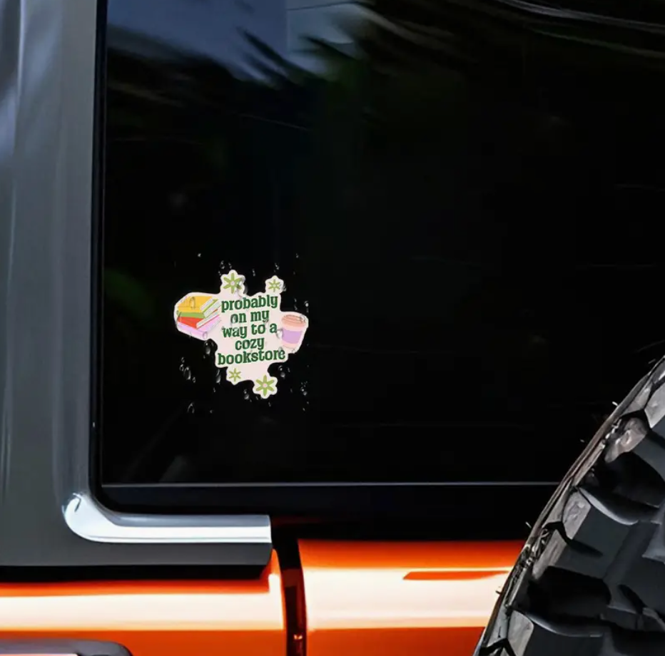 Sticker on a car window with text 'Probably on my way to a bookstore' and rainbow elements.