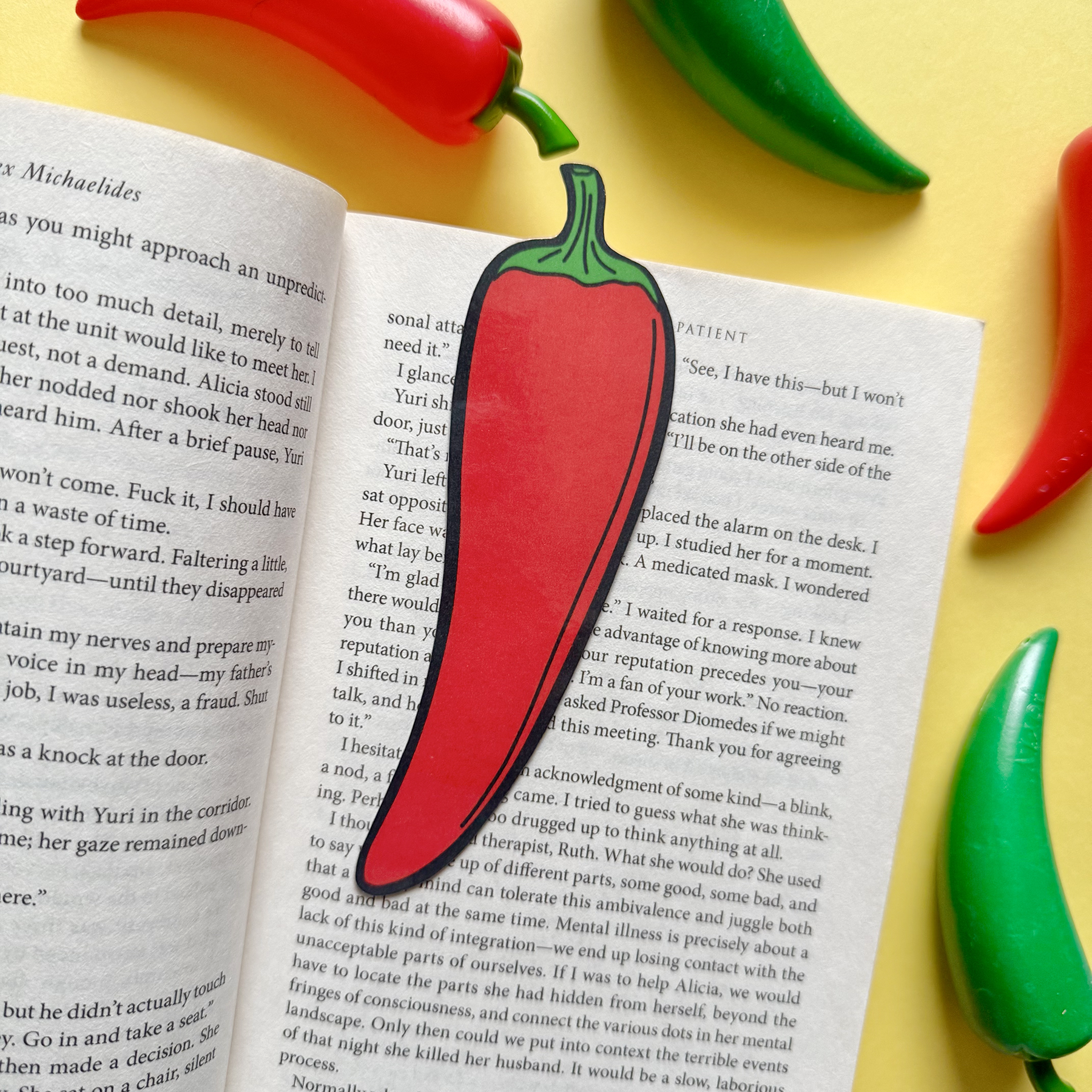 Open book with a red chili pepper-shaped bookmark on a yellow background with green and red chili peppers.