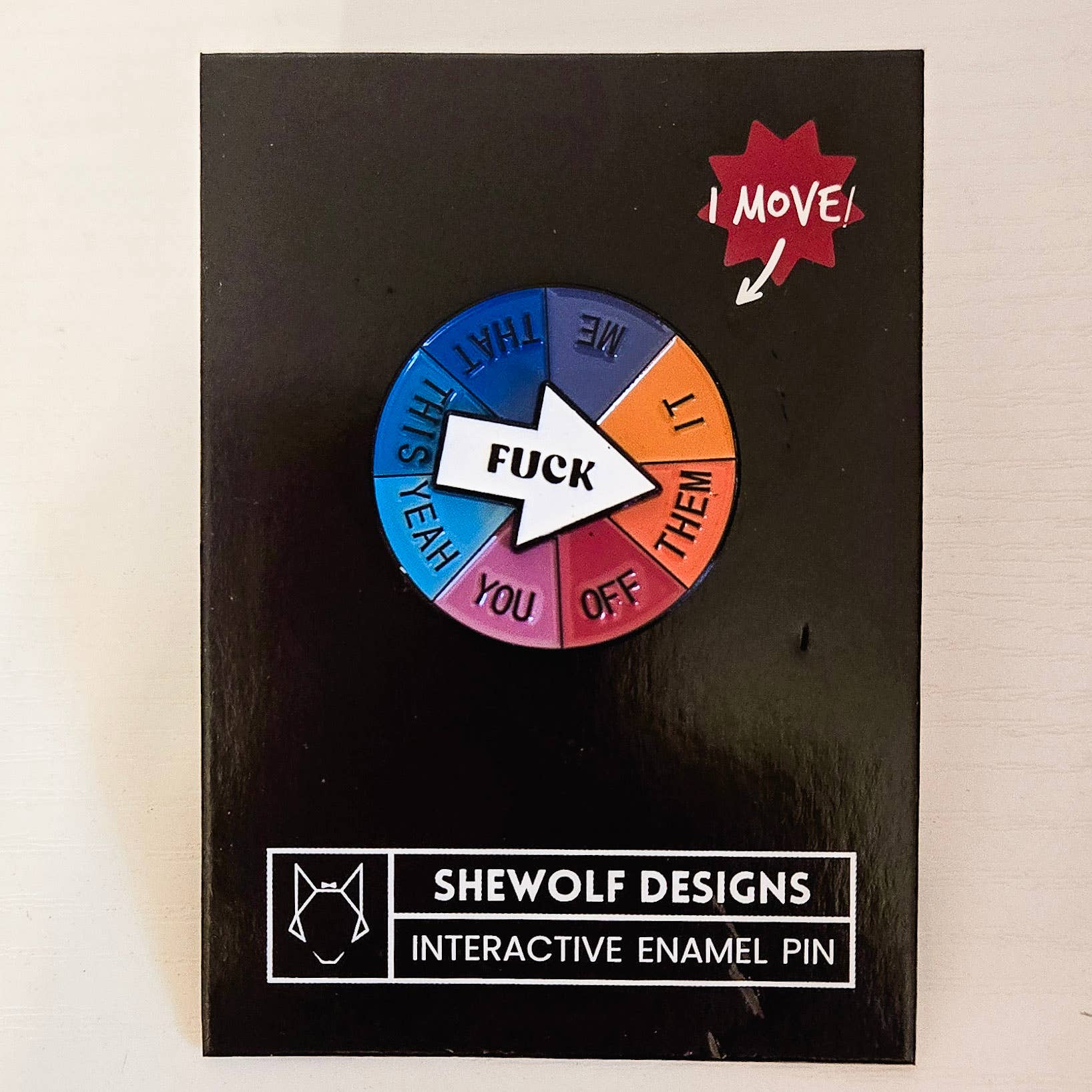 Interactive enamel pin with colorful wheel and text on a black card, branded 'Shewolf Designs'.