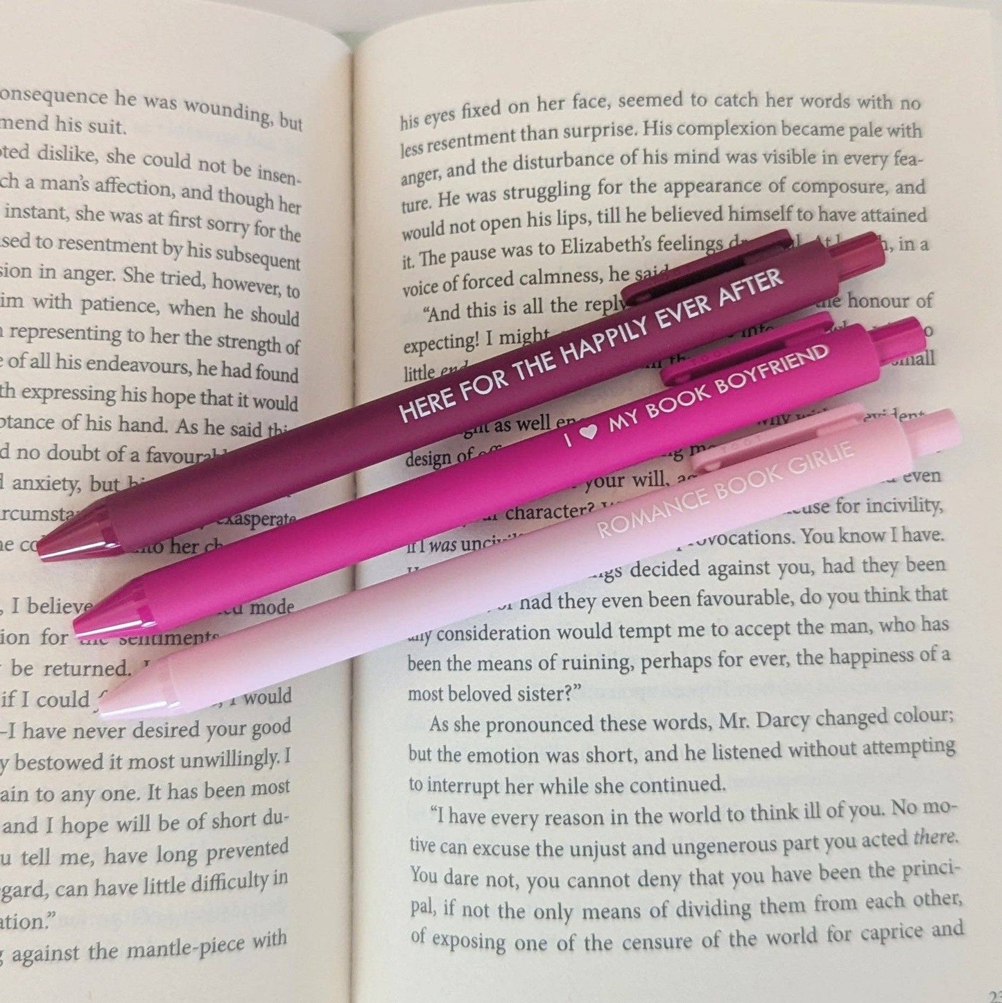 Two pink pens with text on them lying on an open book