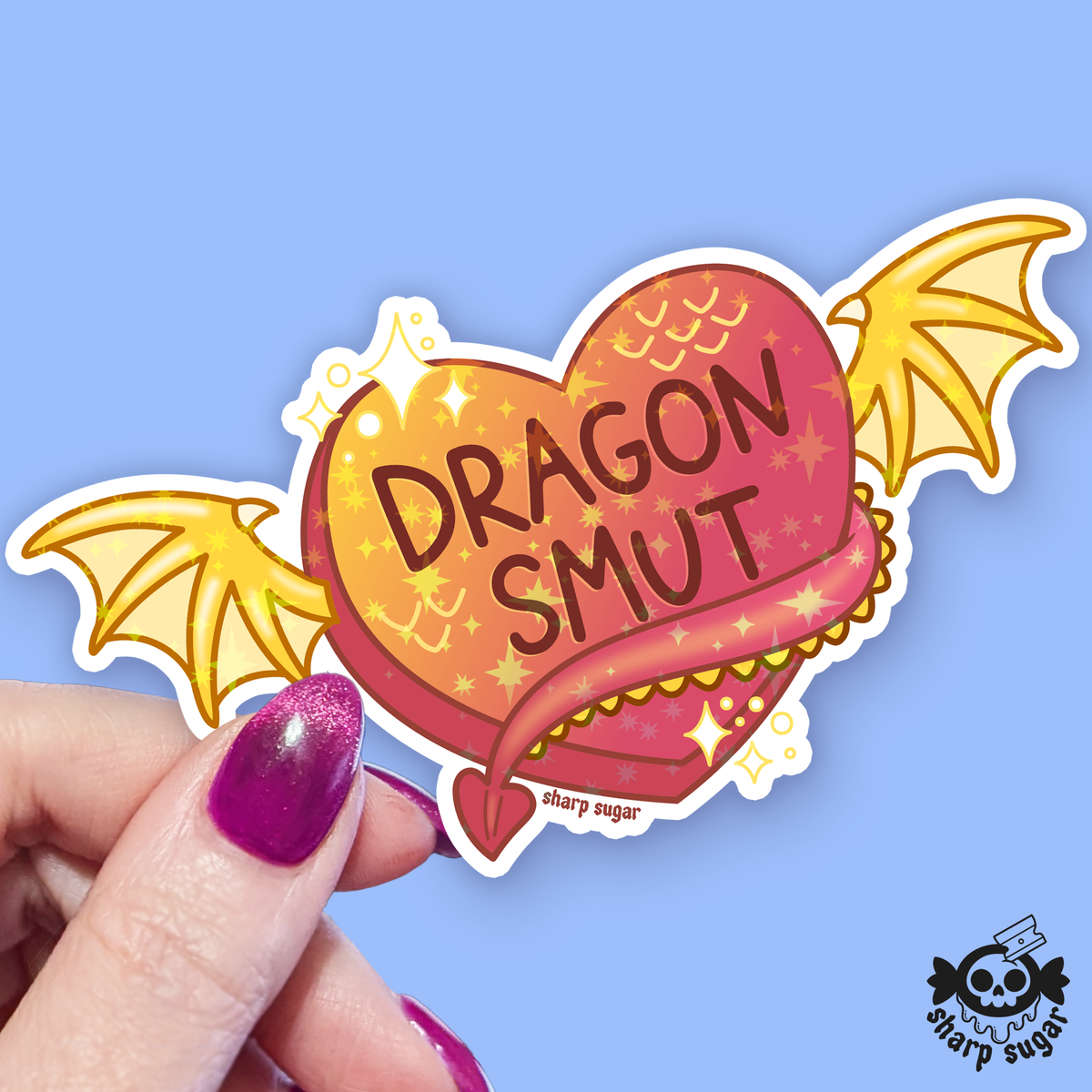 Heart-shaped sticker with 'Dragon Smut' text held by a hand against a blue background