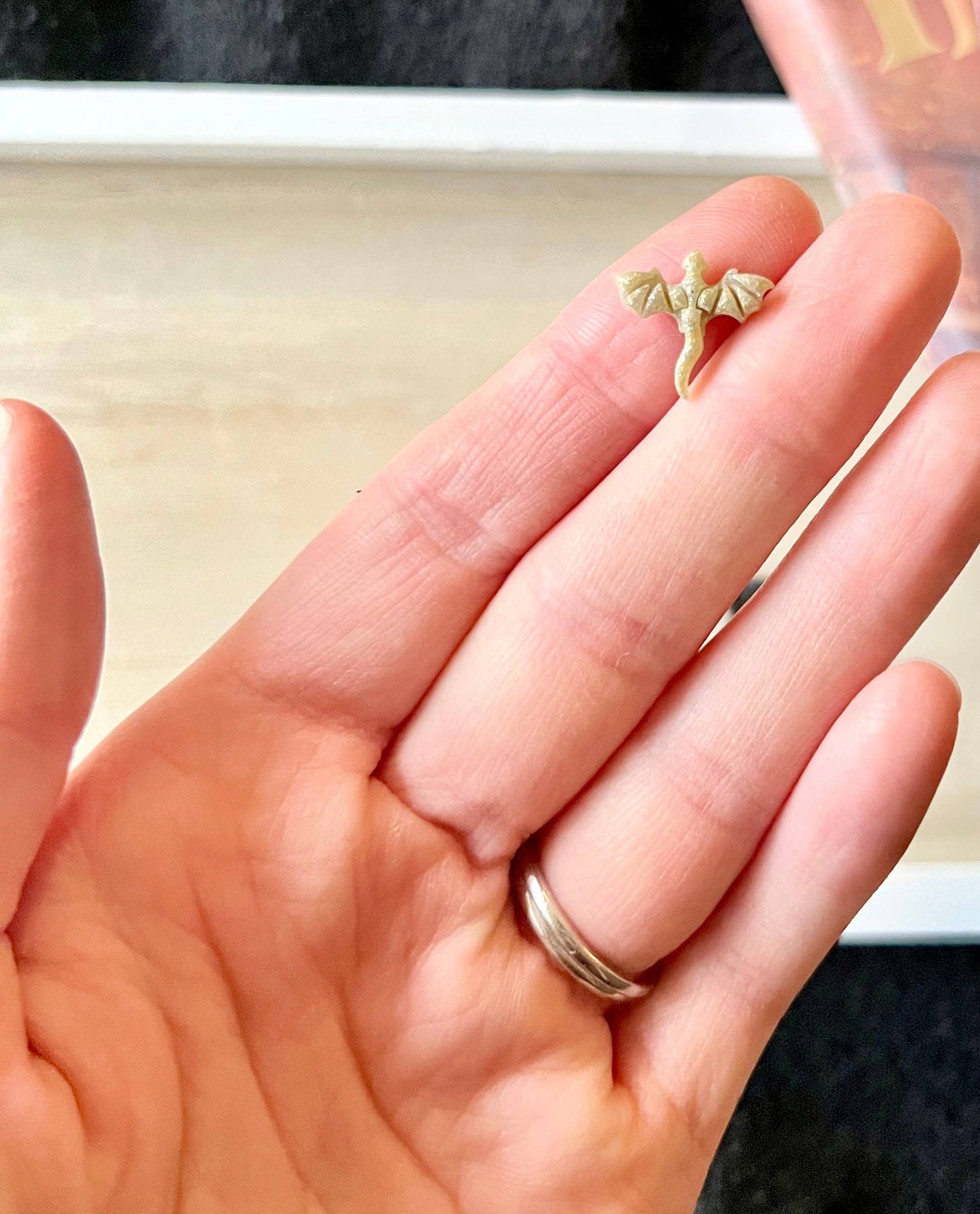 Hand holding a small golden dragon earring with a blurred background