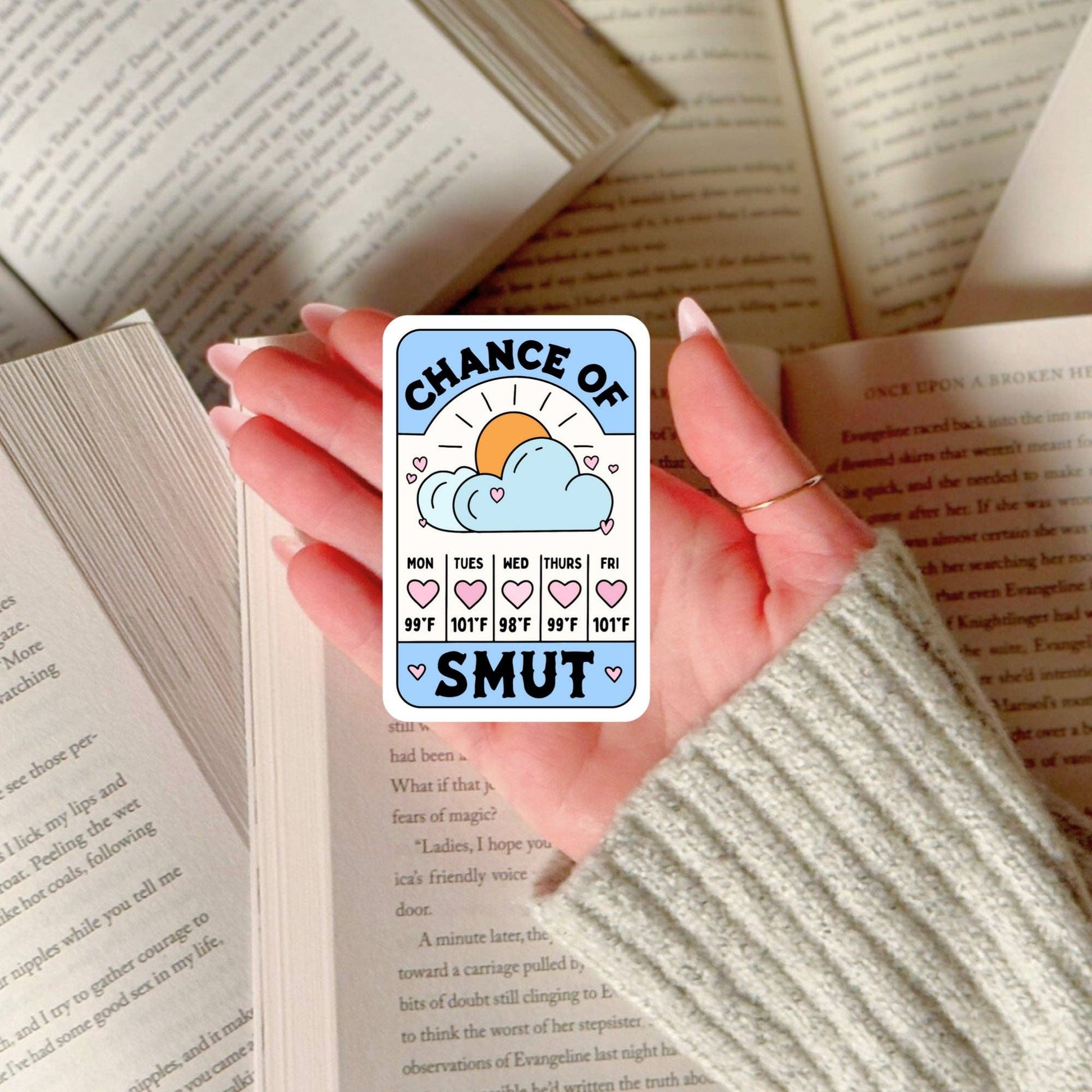 Hand holding a card with 'Chance of Smut' text over an open book