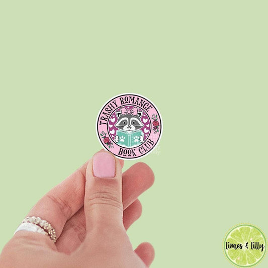Hand holding a round sticker with 'Trinity Romance Book Club' design on a light green background.