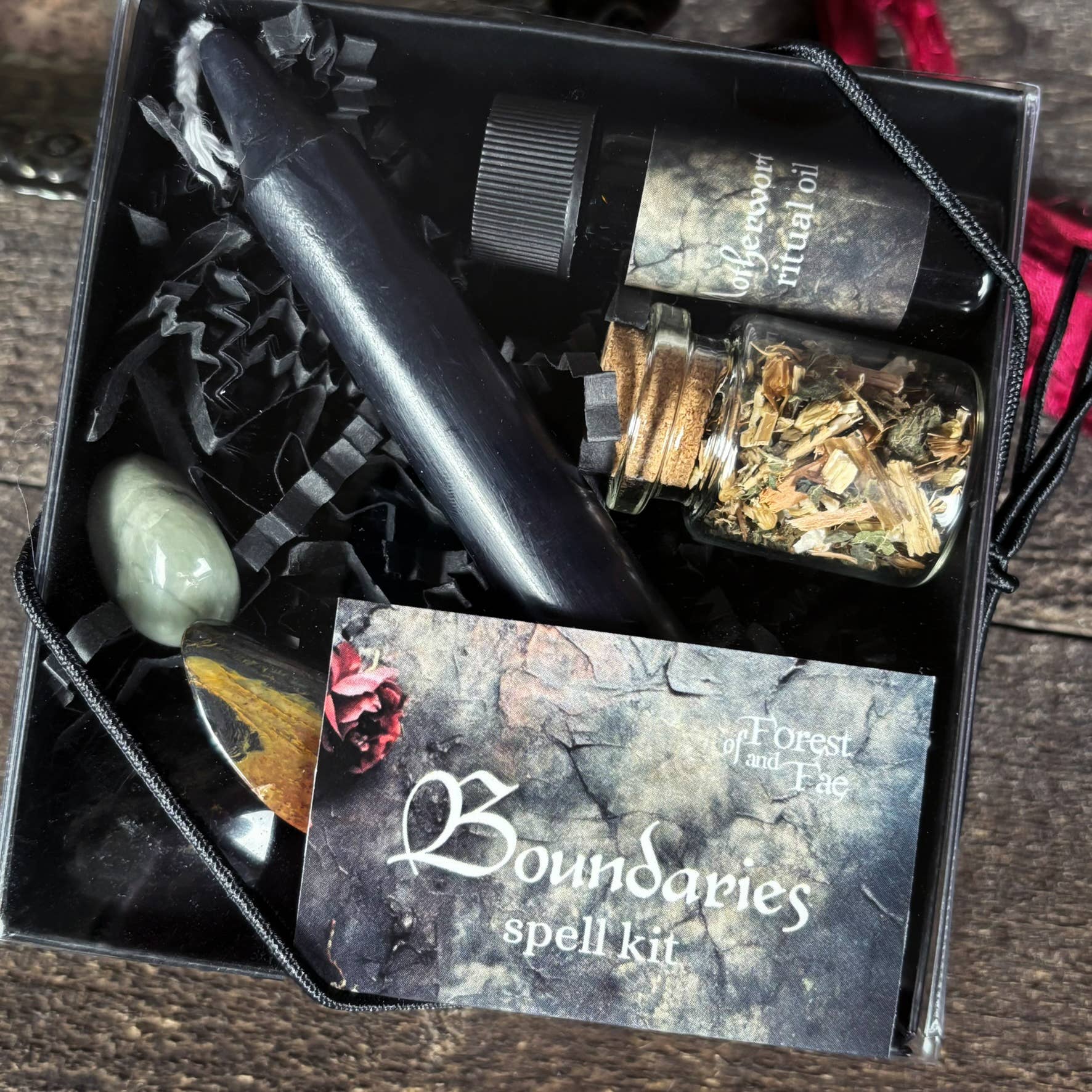 Witchcraft spell kit with candles, stones, and herbs in a box labeled 'Boundaries spell kit'.
