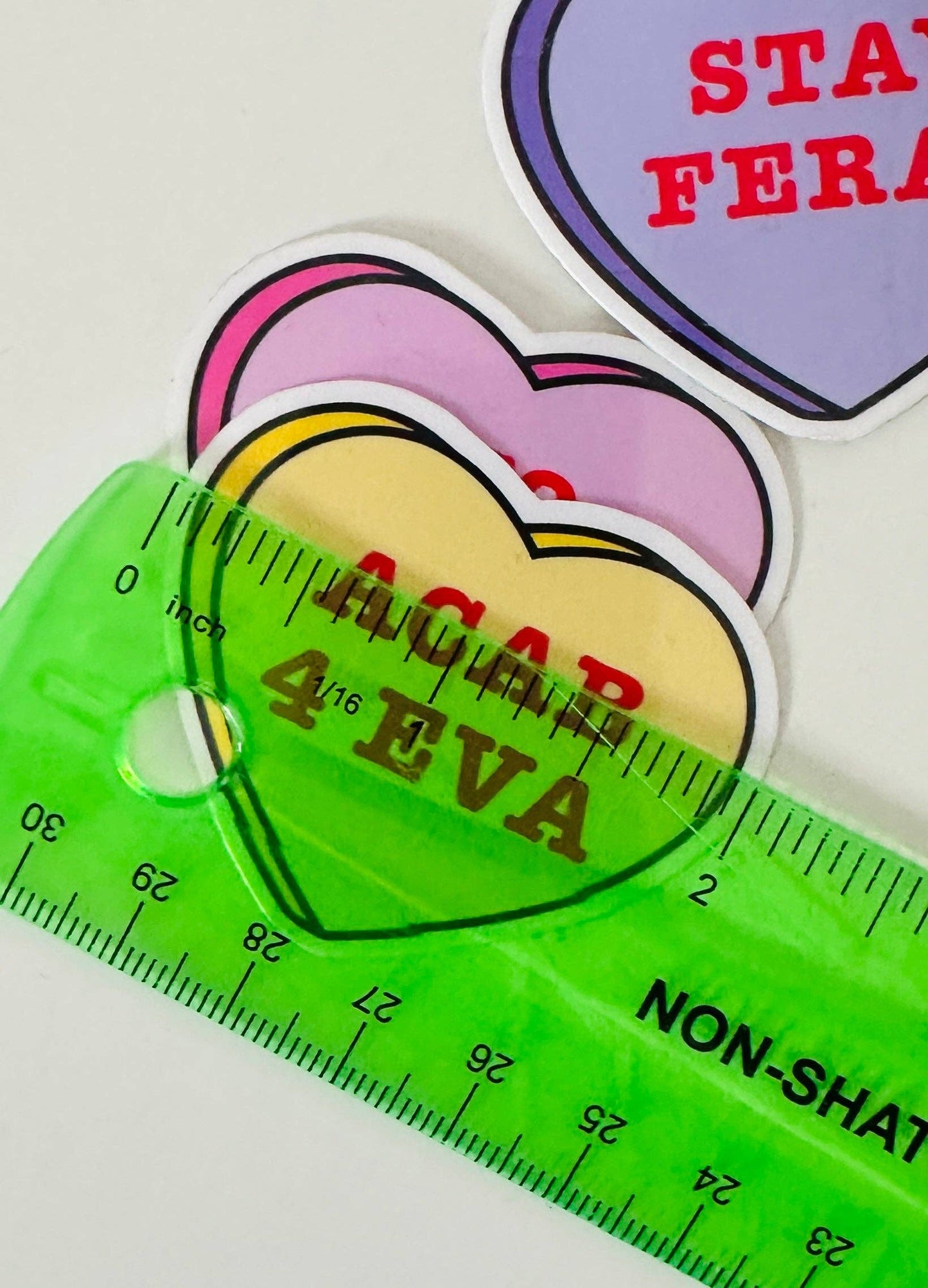 Colorful heart-shaped stickers with text and a green ruler on a white background