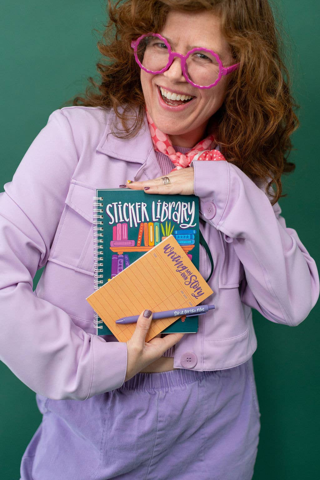 Person holding a notebook and a sticker book against a green background