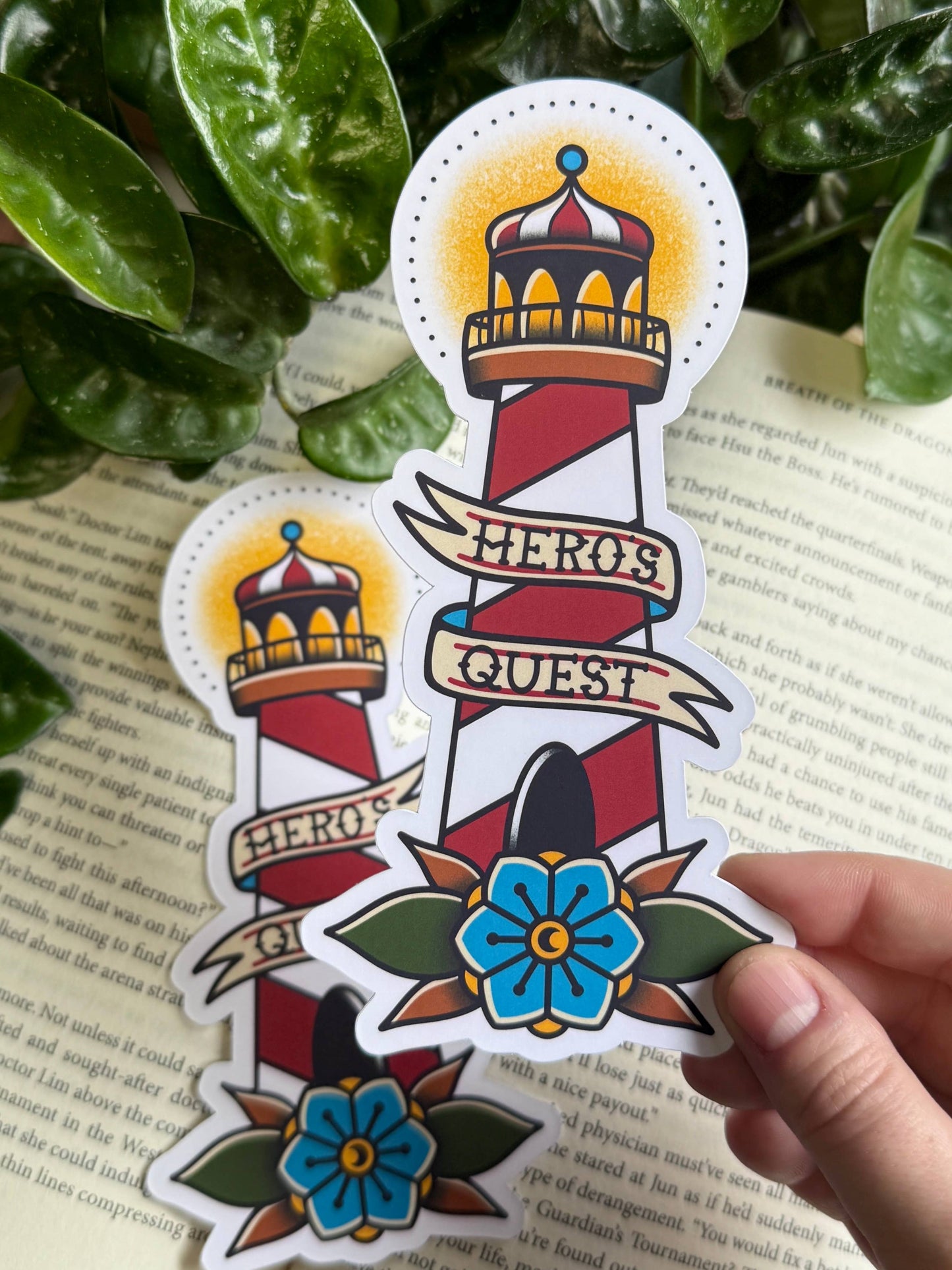 Decorative bookmark with a lighthouse design held over text, surrounded by green leaves.