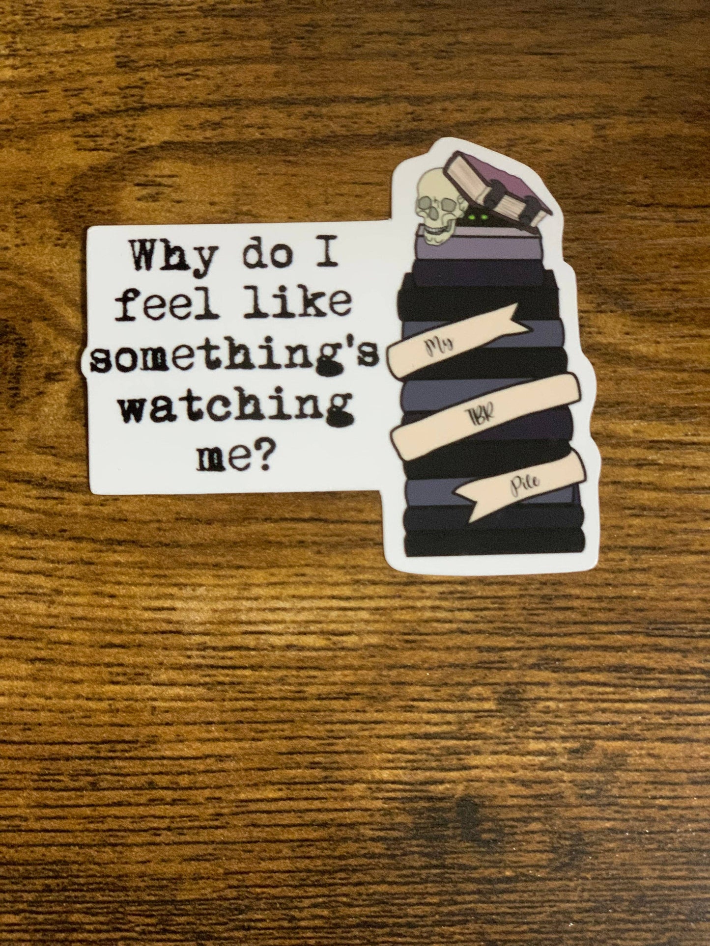 Sticker with text 'Why do I feel like something's watching me?' on a wooden surface