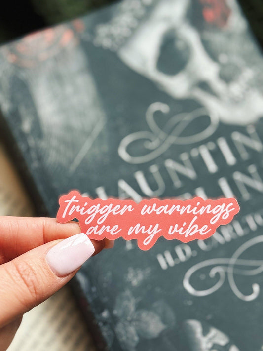 Hand holding a pink sticker with text in front of a book titled 'Hunted'.