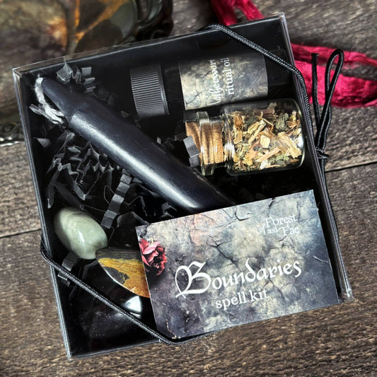 Spell kit with candles, stones, and a card labeled 'Boundaries spell kit' on a wooden surface.