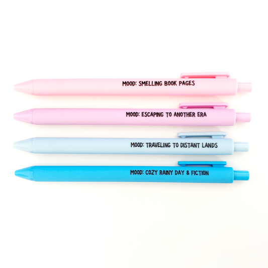 Four pastel-colored retractable pens arranged vertically on a white background, each with a different title printed in black text: 'MOOD: SHELLING BOOK PAGES' in pink, 'MOOD: ESCAPING TO ANOTHER ERA' in light pink, 'MOOD: TRAVELING TO DISTANT LANDS' in light blue, and 'MOOD: COZY RAINY DAY & FICTION' in bright blue.