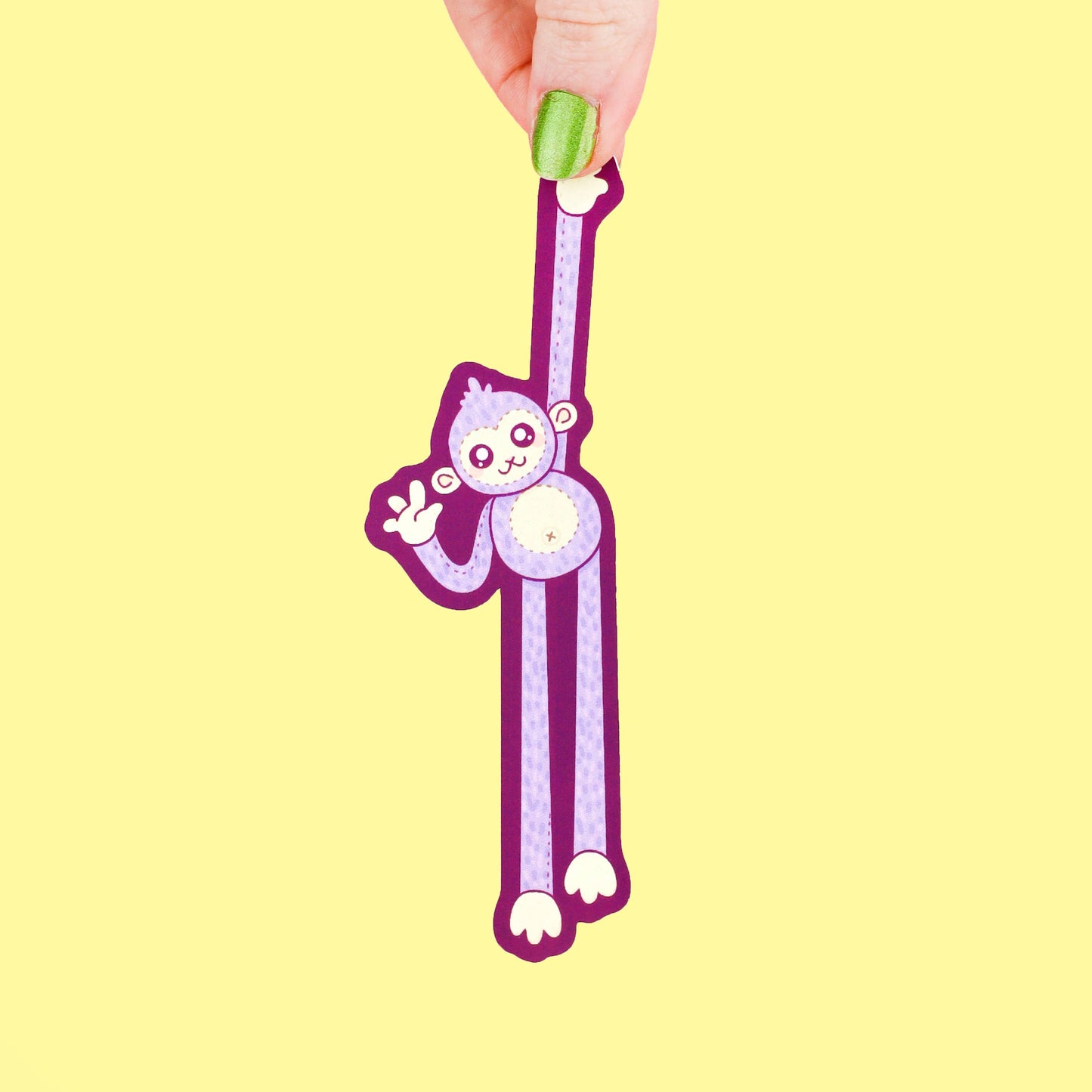 Hand holding a purple monkey-shaped bookmark on a yellow background