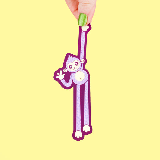 Hand holding a purple monkey-shaped bookmark on a yellow background